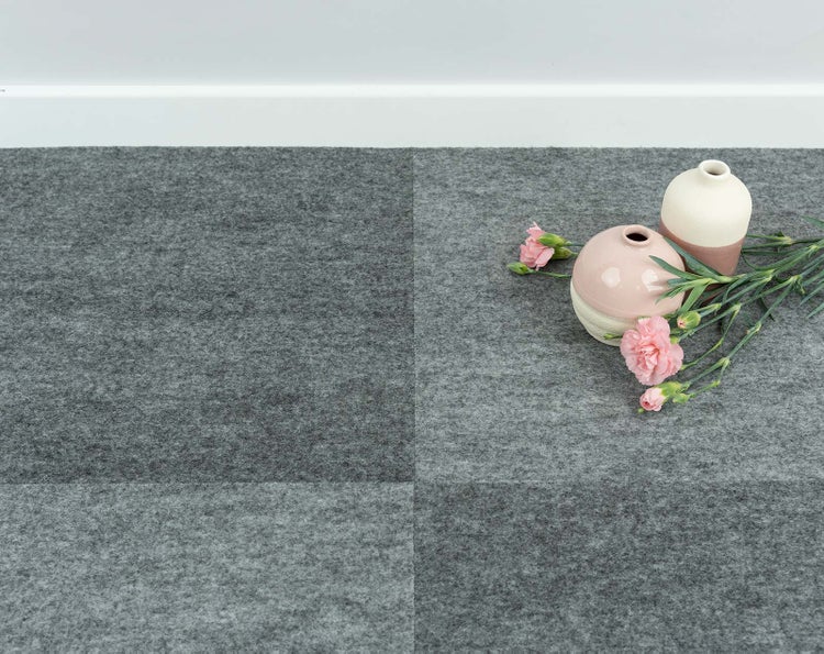 Teppichfliesen in verschiedenen Grautönen in einem Karomuster verlegt mit kleinen Vasen und Blumen als Dekoration.