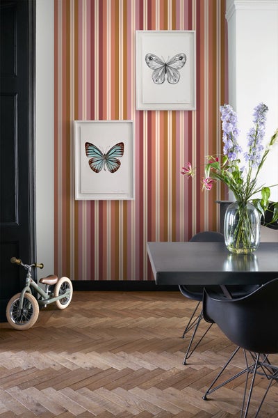 Moderner Wohnbereich mit vertikal gestreifter Tapete, zwei gerahmten Schmetterlingsbildern, einem dunklen Esstisch und Fischgrätparkett.