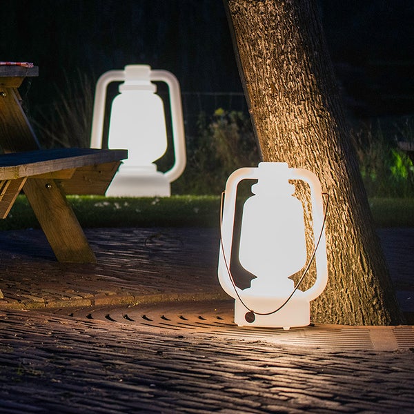 Zwei modern gestaltete, weiß leuchtende Außenleuchten in Form von Laternen auf einer gepflasterten Terrasse im nächtlichen Garten.