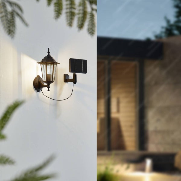 Klassische Solar-Wandlaterne aus Metall und Glas mit separatem Solarpanel, warm leuchtend an einer Hauswand.