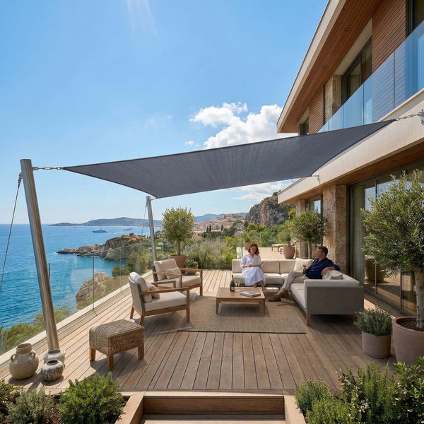 Moderne Terrasse mit einem grauen Sonnensegel über einem Lounge Set aus Sofa und Sesseln auf einem Holzdeck mit Meerblick.