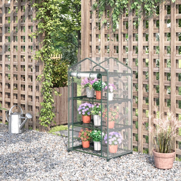 Kleines Foliengewächshaus mit drei Regalböden und transparenter Plane vor einem Holzspalier im Garten auf Kiesboden.