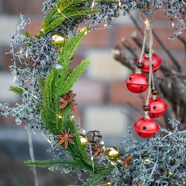 Weihnachtlicher Türkranz mit Tannenzweigen, Sternanis, Kugeln, Lichtern und Glocken