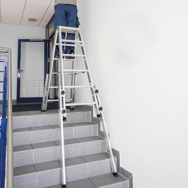 Aluminium-Mehrzweckleiter auf einer Treppe mit einer Person, höhenverstellbare Holme für den Einsatz auf unebenem Untergrund.