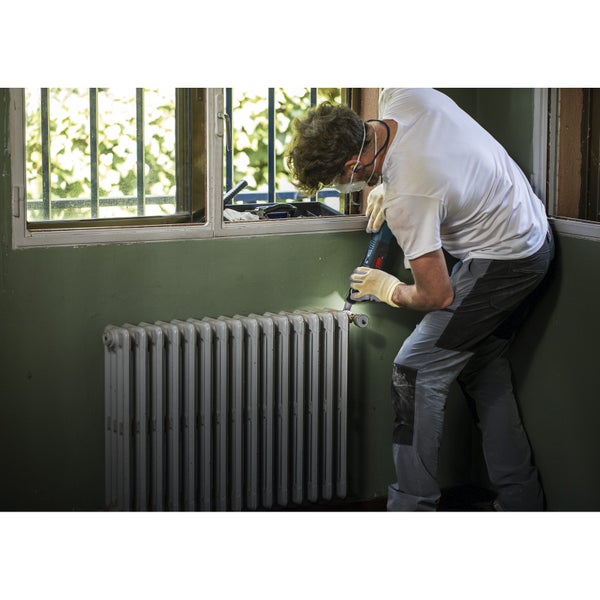 Bediener mit Multitool und Sägeblatt beim Zuschneiden einer Holzbodenoberfläche neben einem Heizkörperrohr