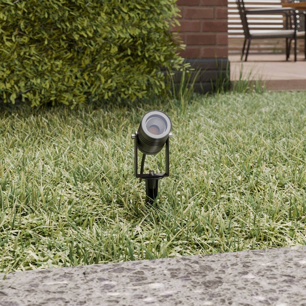 LED-Gartenstrahler mit Erdspieß auf einer Rasenfläche vor einer Hecke und einer Terrasse.