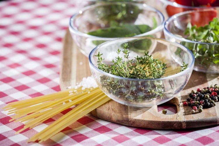 Szene mit Pasta, Kräutern, Gewürzen und Zutaten in Glasschalen auf einem Schneidebrett