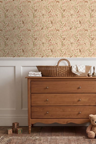 Vliestapete mit floralem Waldmotiv und Tieren im Kinderzimmer über weißer Wandtäfelung und einer Holzkommode.