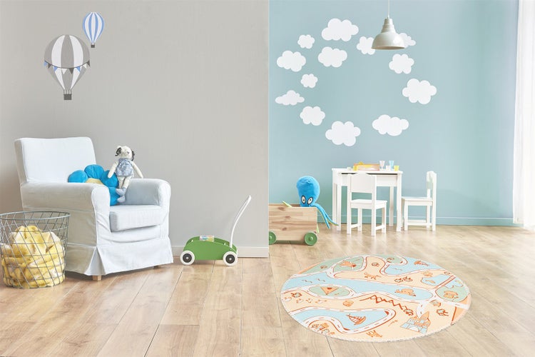 Ein Kinderzimmer mit Spielteppich, Kindersessel, Kindertisch mit Stühlen und Wandaufklebern in Form von Wolken und Heißluftballons.
