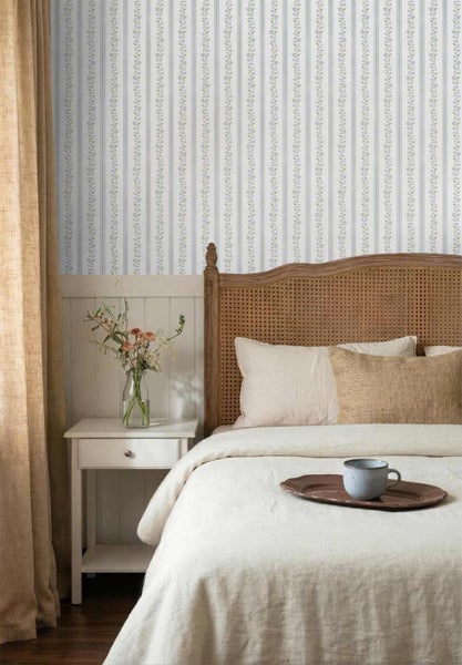 Vliestapete mit feinen floralen Streifen im Schlafzimmer hinter einem Bett mit Rattankopfteil und Nachttisch aus Holz.