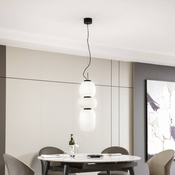 Moderne Pendelleuchte mit drei weißen Glasschirmen übereinander in einem hellen Esszimmer.