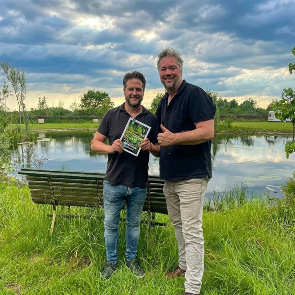 Zwei Männer stehen vor einem großen Gartenteich, einer hält eine Broschüre zur Teichgestaltung und Teichpflege in der Hand.