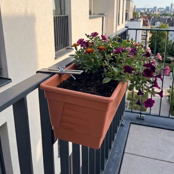 Balkonkasten aus Kunststoff mit Metallhalterung am Geländer befestigt, bepflanzt mit Blumen.