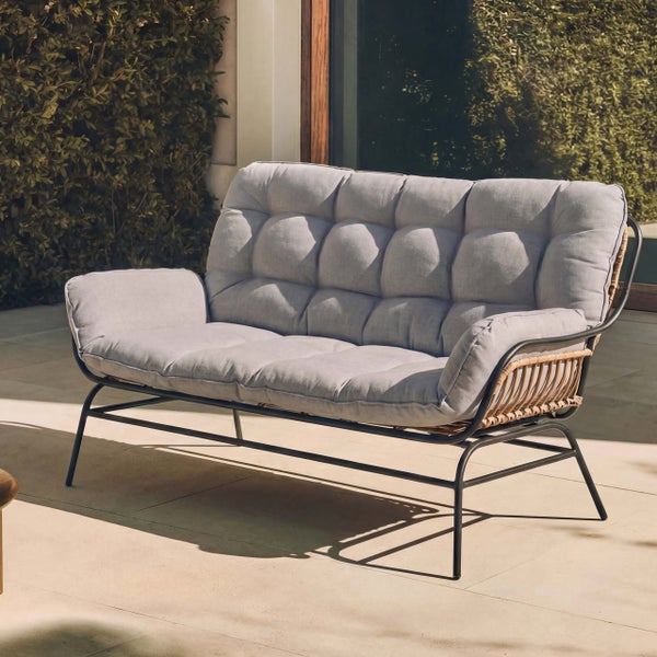 Modernes 2-Sitzer-Gartensofa mit schwarzem Metallgestell, Rattan-Details und dicken, gesteppten grauen Polstern auf einer Terrasse.
