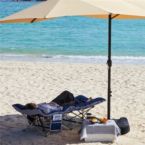 Strandszene mit einer Person auf einer Liege unter einem Sonnenschirm am Meer.