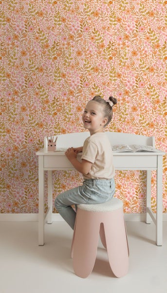 Mädchen sitzt an Schreibtisch vor Blumentapete