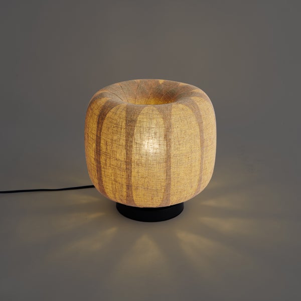 Tischleuchte mit rundem Stoffschirm in Leinenoptik und schwarzem Sockel, eingeschaltet mit warmem Licht.