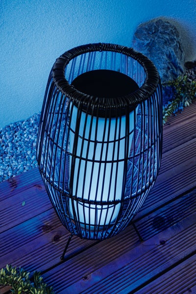 Beleuchtete, fassförmige Außen-Solarleuchte mit schwarzem Drahtgeflecht auf einer Holzterrasse bei Nacht.