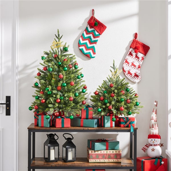 Weihnachtsszene mit zwei Weihnachtsbäumen auf einem Tisch, Weihnachtssocken an der Wand und Geschenken.