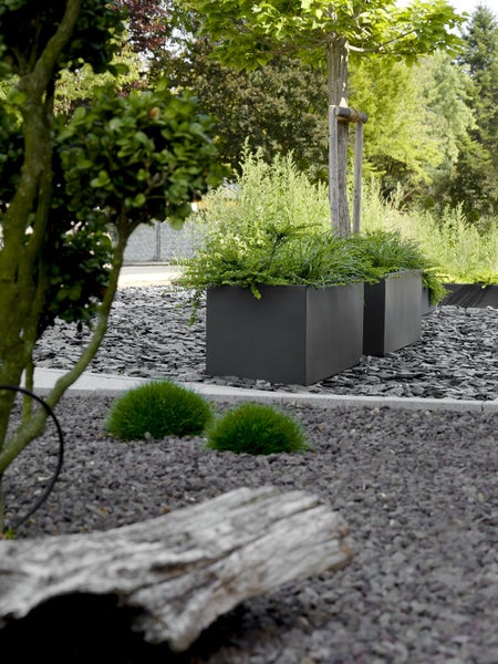Rechteckige Pflanztröge in Anthrazit in einem modernen Garten mit dunklem Schiefersplitt und grünen Pflanzen.