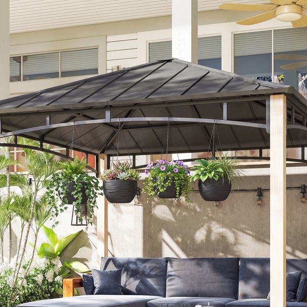 Vier Hängeampeln mit verschiedenen Pflanzen und Blumen, befestigt am Metalldach eines Holzpavillons auf einer Terrasse.