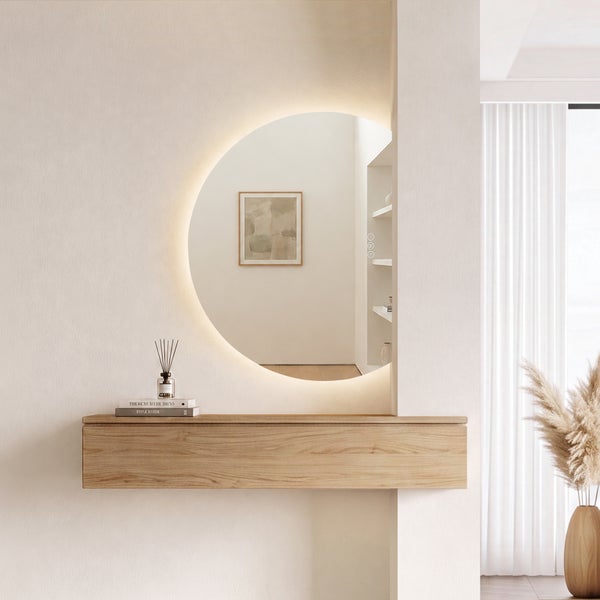 Moderner runder Wandspiegel mit indirekter LED-Beleuchtung über einer schwebenden Holzkonsole in einem hellen, minimalistischen Raum.