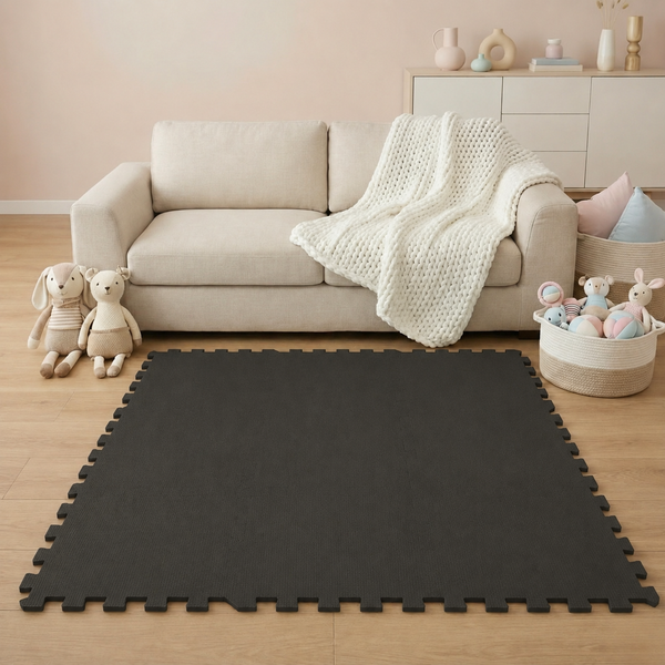 Dunkelgraue Puzzle-Schutzmatte aus Schaumstoff vor einem hellen Sofa in einem Wohnzimmer mit Spielzeug und Kuscheltieren.