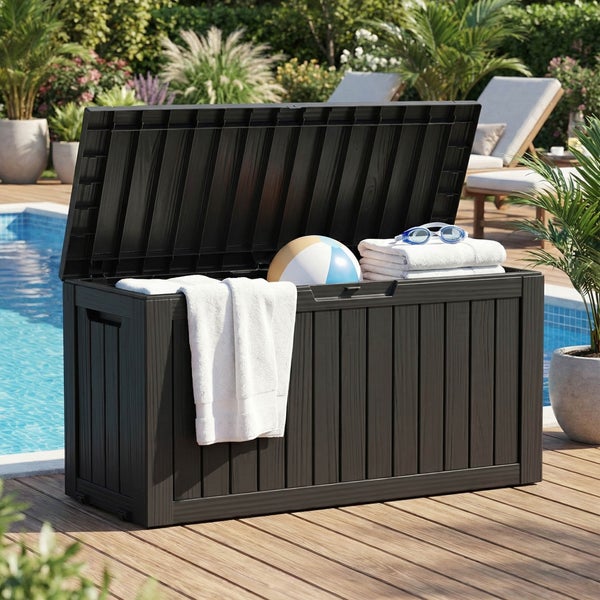 Geöffnete Gartenbox aus Kunststoff in Holzoptik auf einer Holzterrasse am Pool, befüllt mit Handtüchern und einem Wasserball in einem Garten.