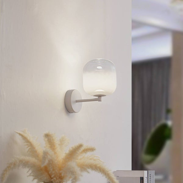 Moderne Wandleuchte mit weißem Metallarm und rundem Glasschirm, an einer Wand montiert und sanft leuchtend.