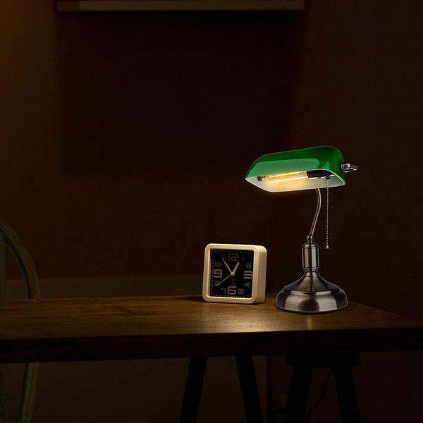 Grüne Schreibtischlampe neben einem Wecker auf einem dunklen Holztisch