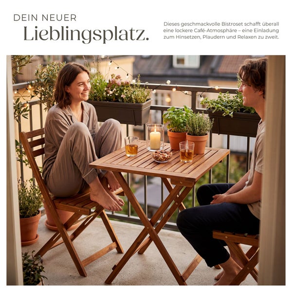 Holz-Bistro-Set bestehend aus Klapptisch und zwei Stühlen auf einem gemütlichen Balkon mit Pflanzen, Lichterkette und zwei Personen.