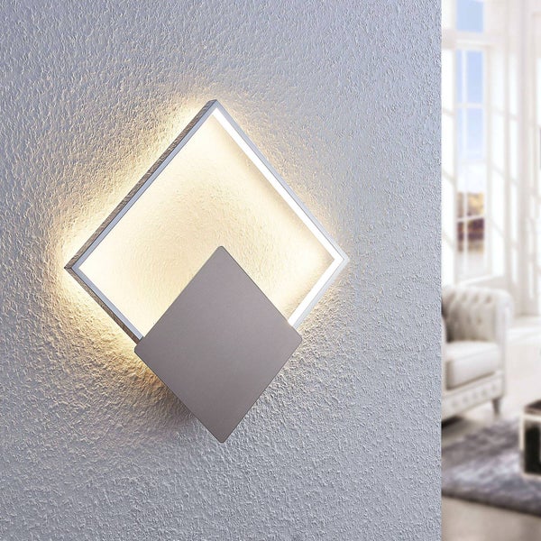 Moderne quadratische LED-Wandleuchte aus Metall, montiert auf einer strukturierten Wand in einem hellen Wohnbereich.