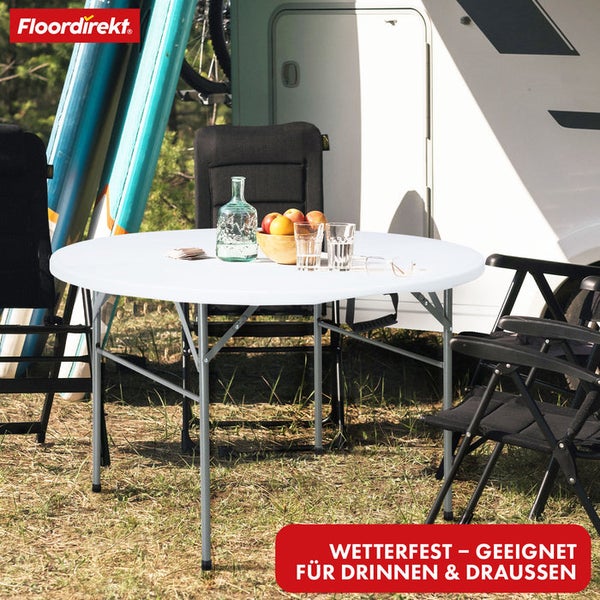 Runder weißer Klapptisch aus Kunststoff mit Metallbeinen in einer Campingszene vor einem Wohnmobil. Wetterfester Tisch für drinnen und draußen.