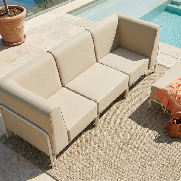 Dreisitzer-Gartensofa mit beigen Polstern und Metallgestell auf einer Terrasse neben einem Pool.