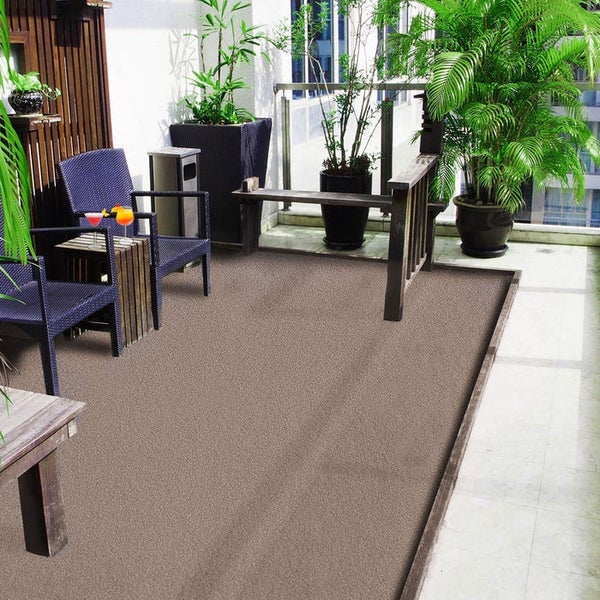 Moderner, heller Balkon mit braunem Outdoor-Teppich, dunklen Korbstühlen, Holzmöbeln und üppigen grünen Topfpflanzen.