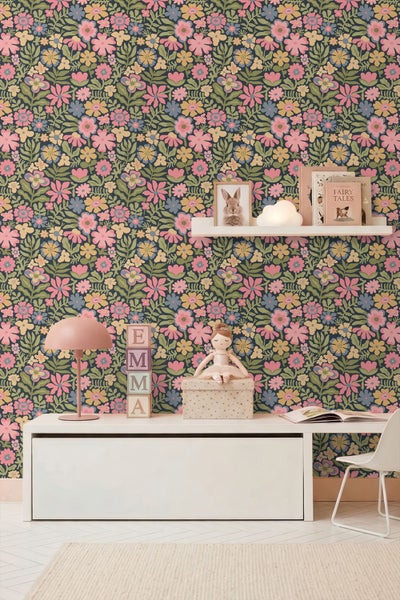 Helles Kinderzimmer mit floraler Vliestapete, weißen Möbeln, Schreibtisch mit Tischleuchte, Holzbausteinen und einem Wandregal mit Dekoration.