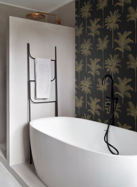 Modernes Badezimmer mit freistehender Badewanne, Handtuchhalter, goldener Regendusche und Tapete mit Palmenmuster.