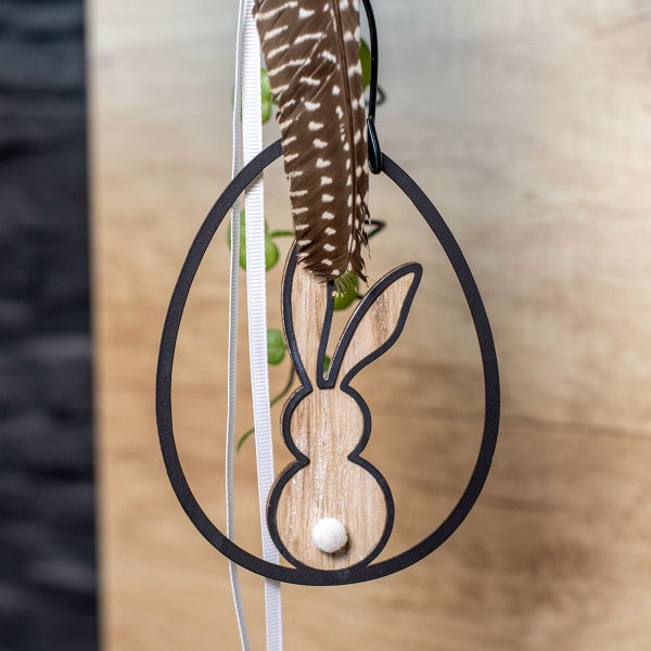 Dekoratives Osterei mit Hasenmotiv, Feder und Bändern zum Aufhängen.