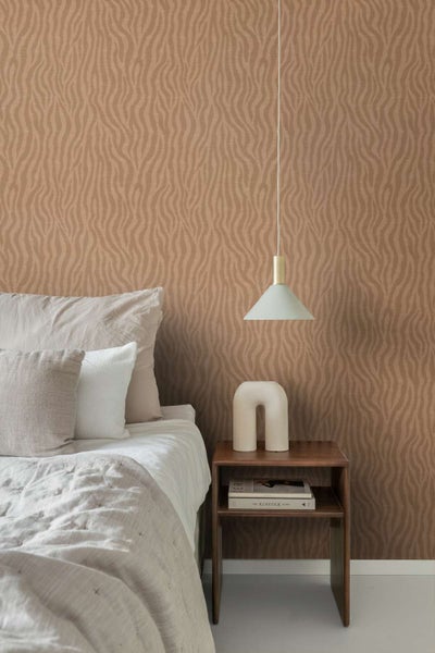 Schlafzimmer mit brauner Vliestapete mit wellenförmigem Muster, kombiniert mit einem Holznachttisch, einer Designerleuchte und hellem Bettzeug.