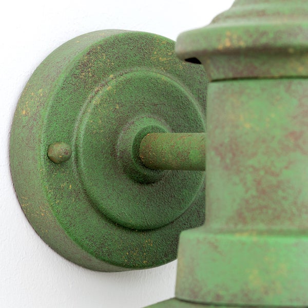 Detailaufnahme einer Wandhalterung für Außenleuchten aus Metall mit einer grünen Patina-Oberfläche.