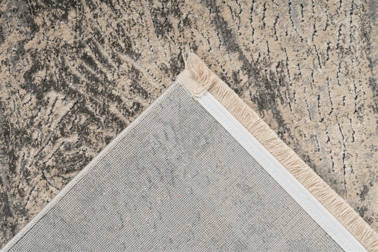 Grauer Teppich mit abstraktem Muster, Fransen und sichtbarer gewebter Rückseite an der Ecke.