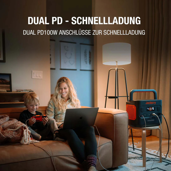 Jackery Powerstation mit 100 Watt Schnellladefunktion lädt Laptop und Konsole im Wohnzimmer auf, während eine Frau und ein Kind auf dem Sofa sitzen.