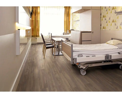 Modernes Krankenzimmer mit Boden in Holzoptik, Krankenhausbett, Tisch, Stühlen und geometrischer Tapete in hellem, organisiertem Ambiente.