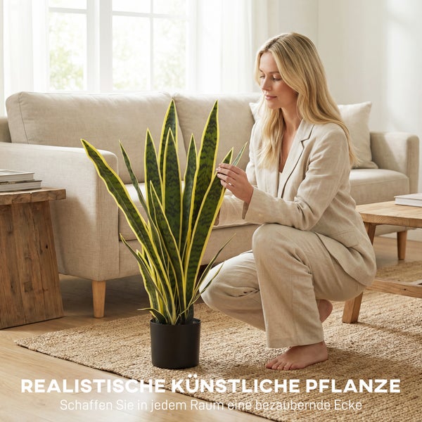 Realistische künstliche Bogenhanf-Pflanze im Topf in einem hellen Wohnzimmer mit Sofa, Holztisch und Juteteppich.