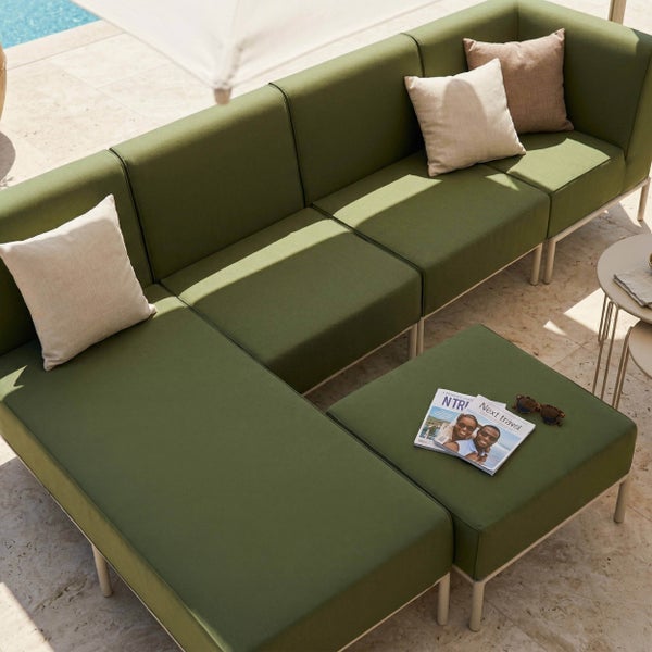 Modernes Garten-Lounge-Set mit grünen Polstern, bestehend aus Ecksofa und Hocker auf einer Steinterrasse am Pool.