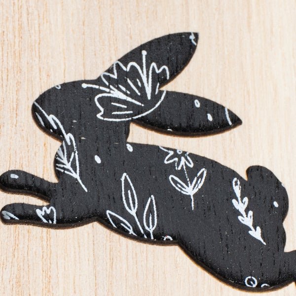 Deko-Osterhase aus Holz, springend, schwarz mit weißem Blumenmuster.