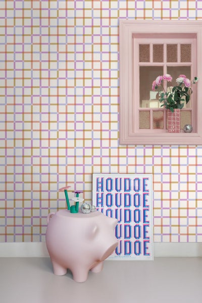 Vliestapete mit buntem Karomuster in einem Zimmer mit rosa Fensterrahmen, einer Blumenvase und einer rosa Schweineskulptur.
