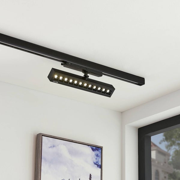 Modernes, schwarzes Schienensystem mit einem rechteckigen LED-Strahler an der Decke in einem hellen Raum mit Fenster und Bild an der Wand.