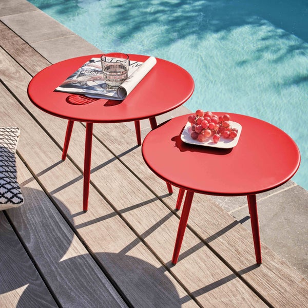 Zwei runde rote Beistelltische aus Metall auf einer Holzterrasse am Pool mit Weintrauben, einem Glas Wasser und einer Zeitschrift.