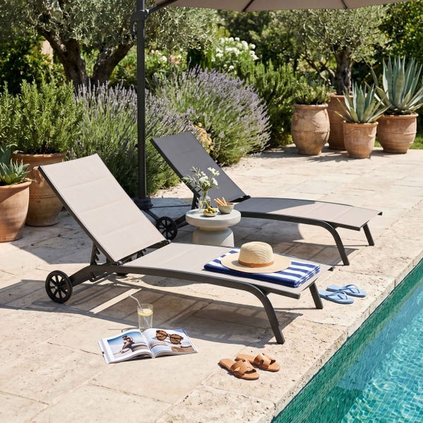 Zwei verstellbare Gartenliegen mit Rollen auf einer Steinterrasse am Pool, umgeben von Pflanzen in Terrakottatöpfen und einem Sonnenschirm.